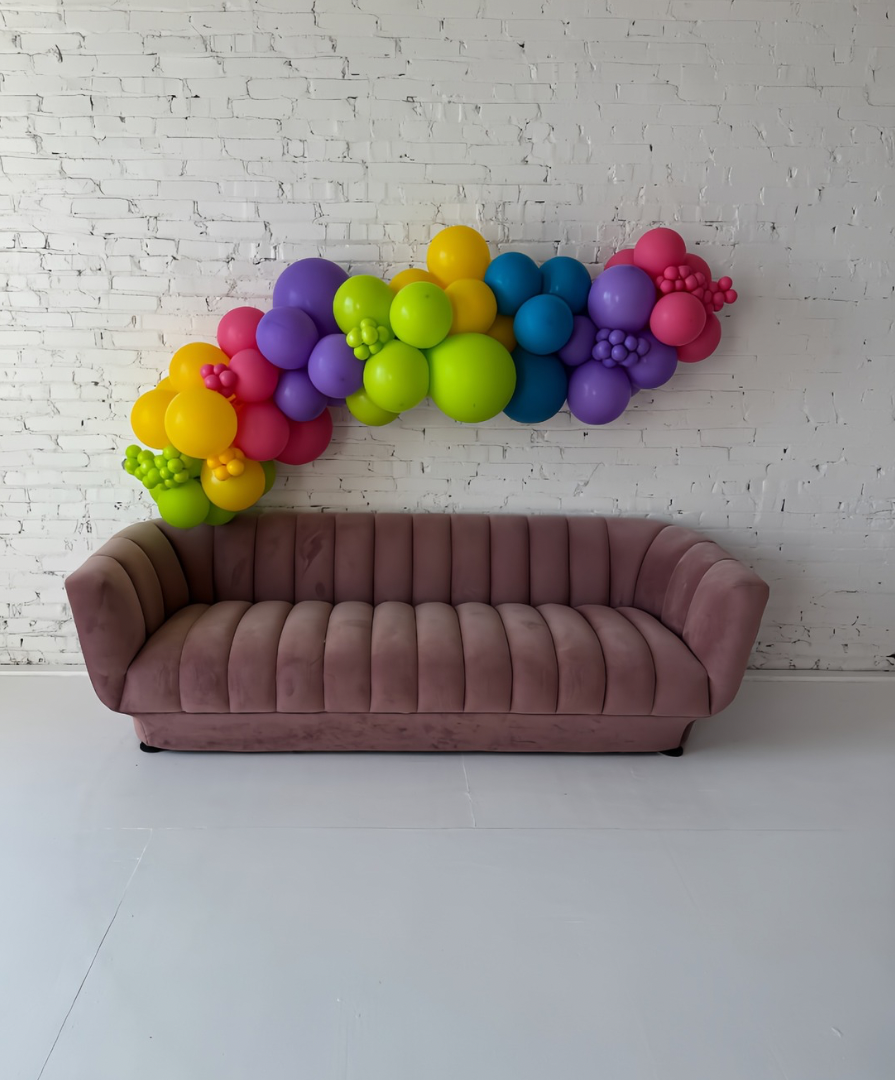 Vibrant balloon garland installation paired with a mauve sofa, designed by Lady With The Balloons in Leawood, Kansas — stylish backdrop for parties, showers, and special events.