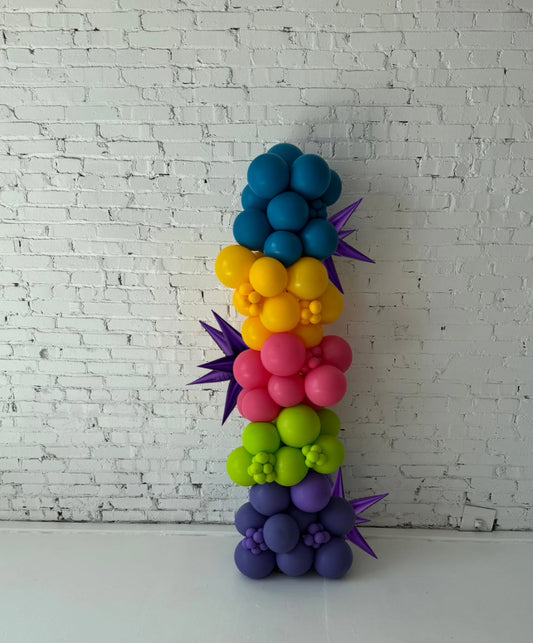 Freeform balloon column installation by Lady With The Balloons in Leawood, Kansas — featuring vibrant rainbow colors, layered textures, and metallic purple starburst accents for modern event décor.
