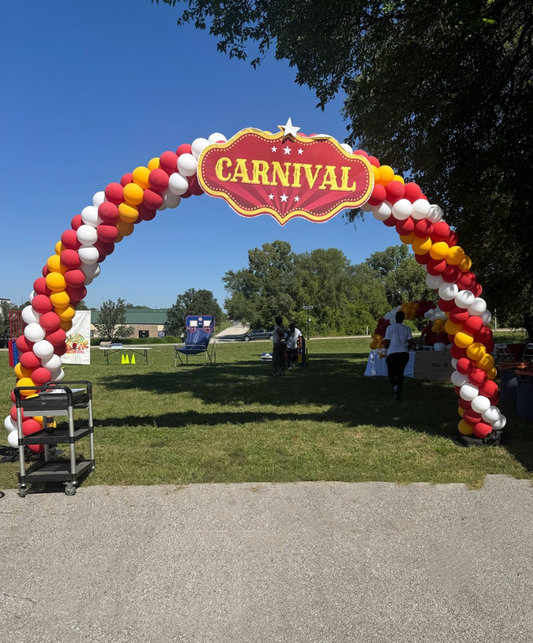 Large classic balloon arch installation by Lady With The Balloons in Leawood, Kansas — outdoor carnival-themed event setup with red, yellow, and white balloons.
